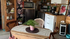 Ein Essbereich mit Holztisch, Stühlen, einer Topfpflanze, einer Mikrowelle und einem Kühlschrank.