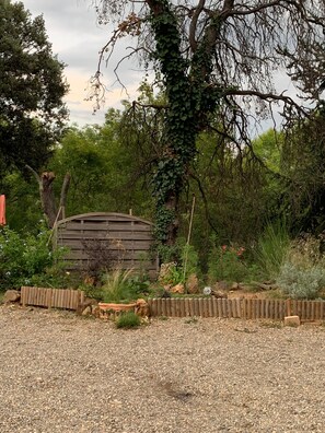 A rustic wooden structure surrounded by gravel, greenery, and a wooden fence. - The Chalet with Private Garden and Wi-Fi (Taillet)