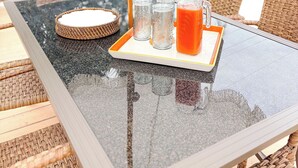 Ett glasbord med ett bricka som innehåller en glaskaraff och glas, flätade stolar och ett vitt parasoll.