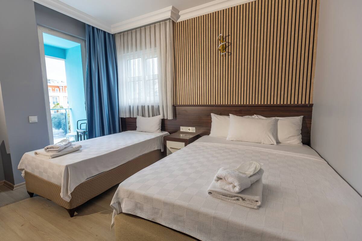 A hotel room with two beds, a wooden headboard, a nightstand, and a view of the outside.