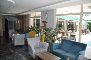 A hotel lobby with seating areas, a clock on the wall, and large windows.