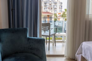 A room with a dark-colored armchair, a small table, and a view of a balcony with a chair and a table. - Citrus Urban (Konyaaltı)