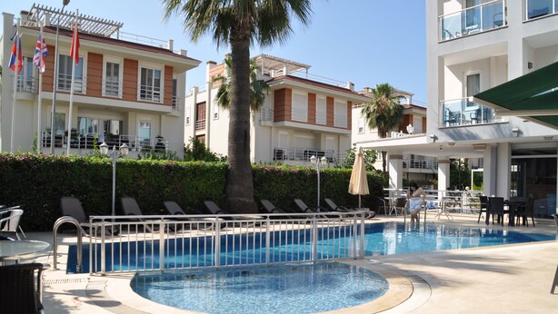A swimming pool with a 30 cm depth marker, lounge chairs, and a building with balconies. - Citrus Urban (Konyaaltı)