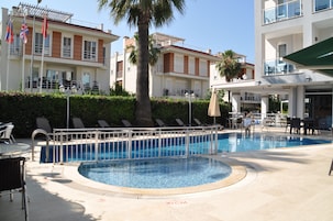 Piscina com indicador de profundidade de 30 centímetros, cadeiras de espreguiçadeira e um edifício com varandas.