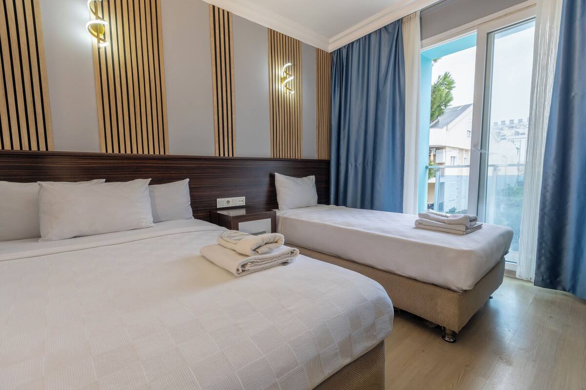 A hotel room with two beds, a wooden headboard, a nightstand, and a view of the outside.