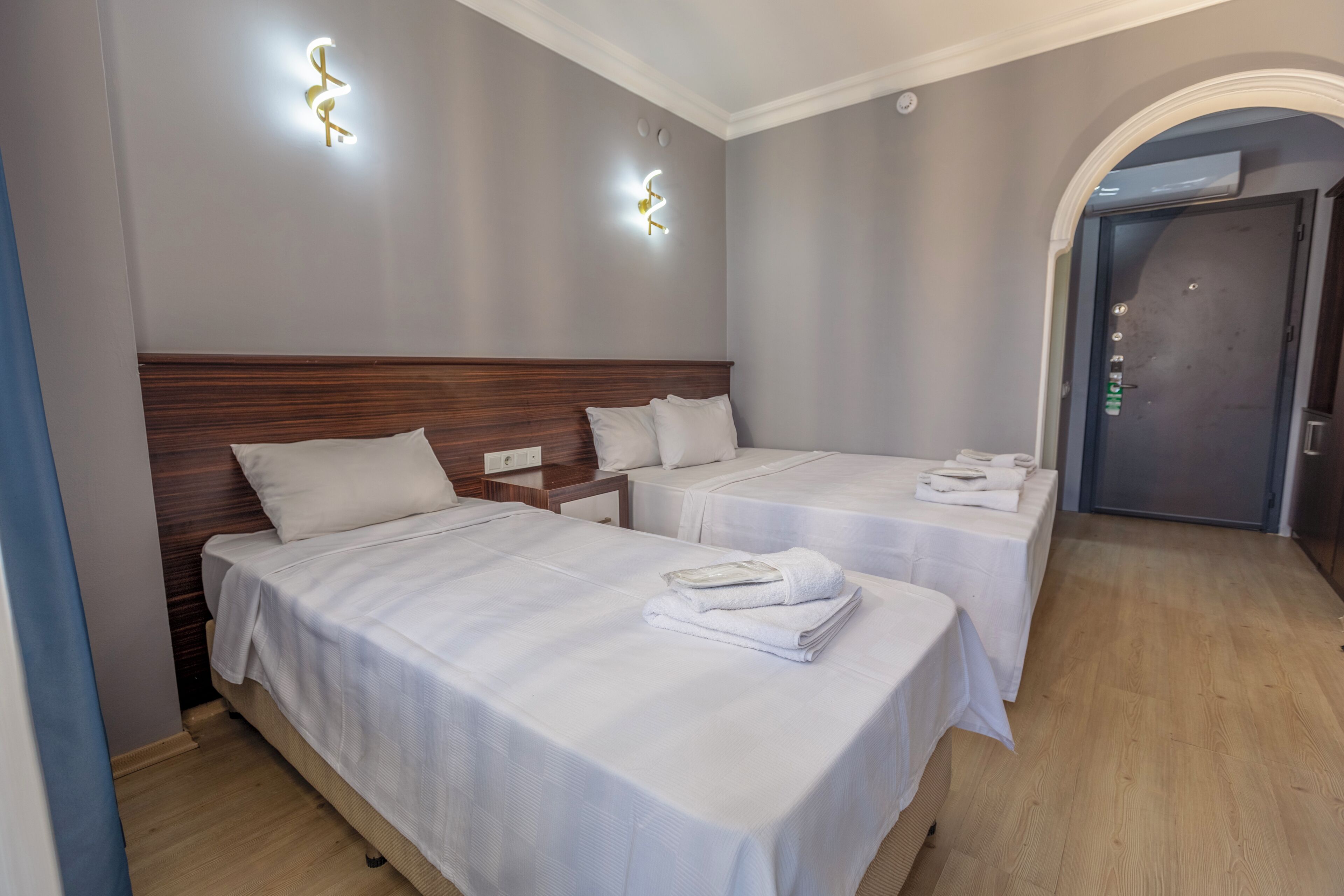 A hotel room with two beds, a wooden headboard, a nightstand, and a door with a handle.