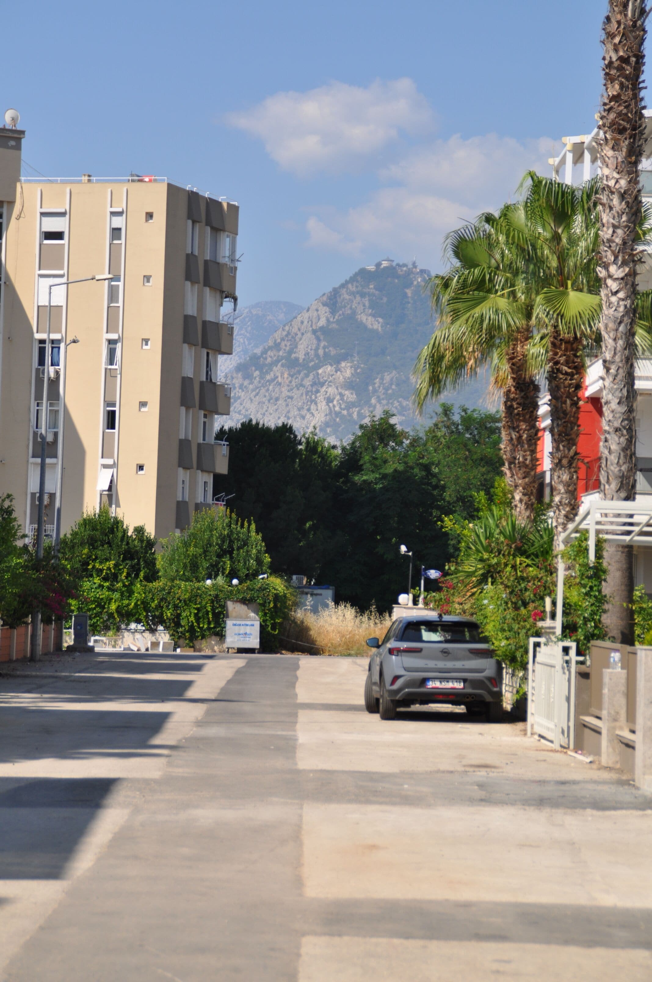 A multi-story building with balconies, a parked car, and a mountain in the background.