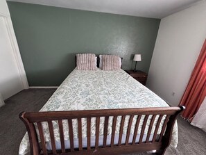 Ein Schlafzimmer mit einem Bett, einem Nachttisch, einer Lampe und einer grünen Wand.