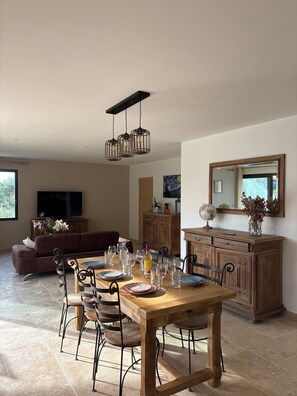 A dining area with a wooden table and chairs, a sofa, a TV, and a cabinet with a globe and decorative items. - NEW 2026:COMFORTABLE AIR-CONDITIONED HOUSE, PRIVATE POOL, CLOSE TO THE  VILLAGE (Sablet)