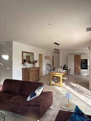 A modern living room with a brown sofa, a dining table with chairs, a kitchen area, and a large mirror on the wall. - NEW 2026:COMFORTABLE AIR-CONDITIONED HOUSE, PRIVATE POOL, CLOSE TO THE  VILLAGE (Sablet)