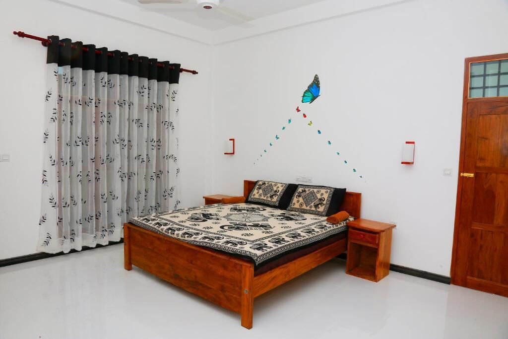 Quarto com cama de madeira, colcha estampada, decoração de borboleta na parede e uma porta.