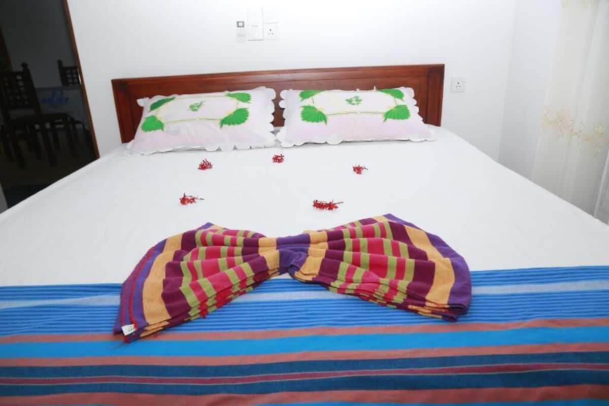 A bed with a striped bedspread, two pillows with a leaf pattern, and a colorful towel arranged on the bed.