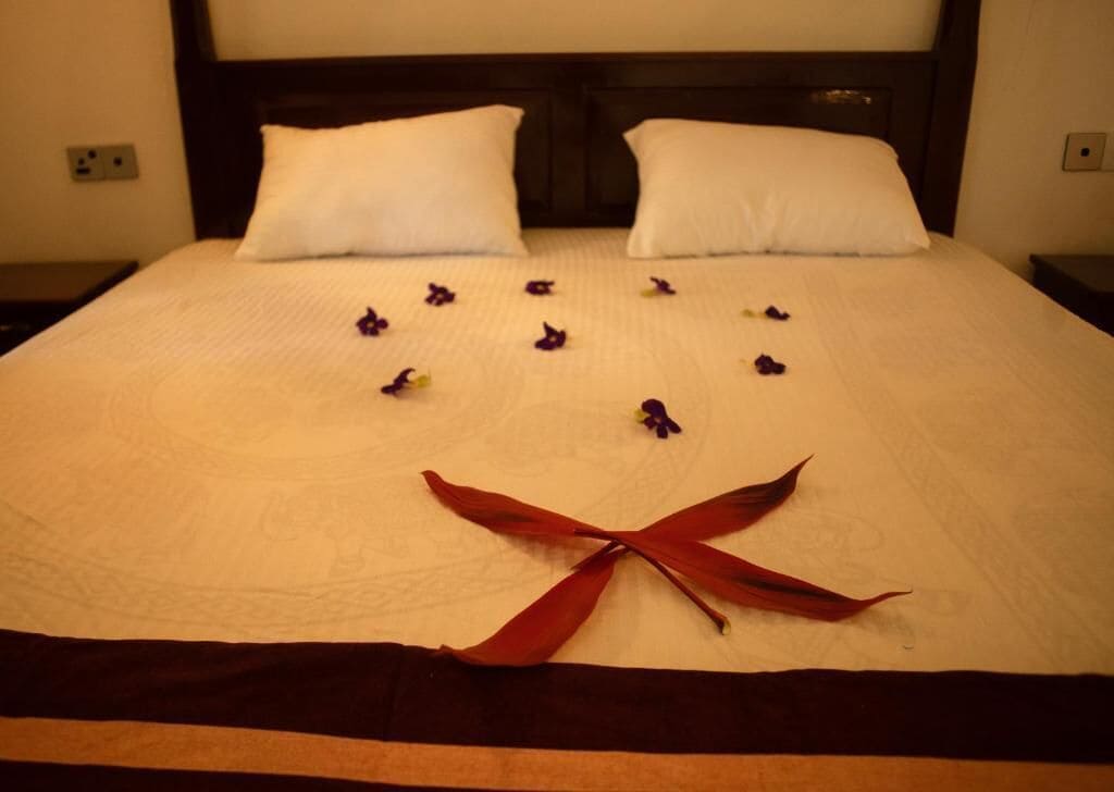 A neatly made bed with white pillows, a dark headboard, and a decorative arrangement of flowers and ribbons on the bedspread.