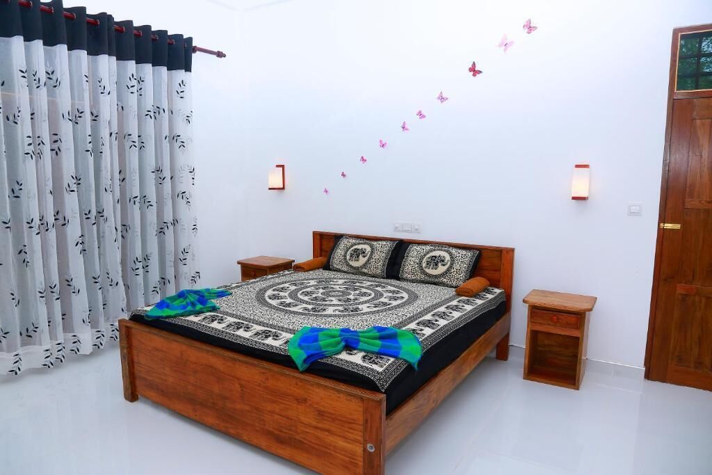 A bedroom with a wooden bed, a small bedside table, a nightstand, a curtain with a leaf pattern, and a wall with butterfly decals.