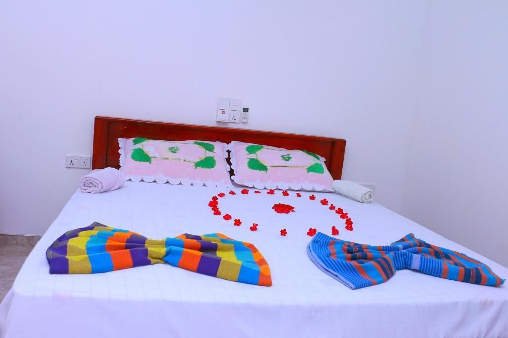 Ein Bett mit weißer Bettdecke, zwei Kissen mit grünen Blattmustern, einer farbenfrohen Streifenwolldecke und einem weißen Kissen.