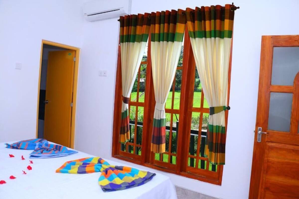 A room with a bed, a window with curtains, a door, and an air conditioning unit.