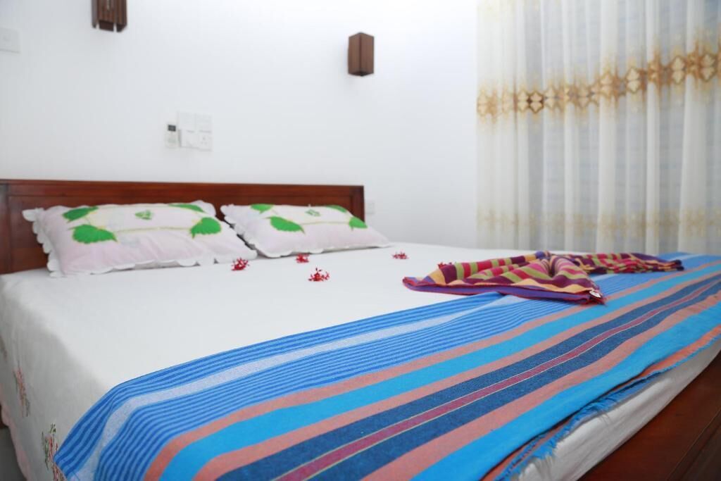A bed with a striped blanket, pillows with green leaf patterns, and a colorful striped blanket on the floor.