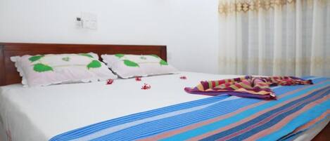 A bed with a striped blanket, pillows with green leaf patterns, and a colorful striped blanket on the floor.