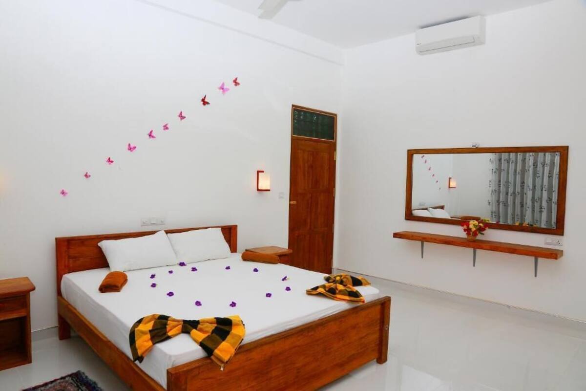 A bedroom with a wooden bed, a bedside table, a mirror, and a wall-mounted shelf.