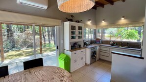 A modern kitchen with a built-in washing machine, a dining area with a round table, and large windows offering a view of the outdoors.