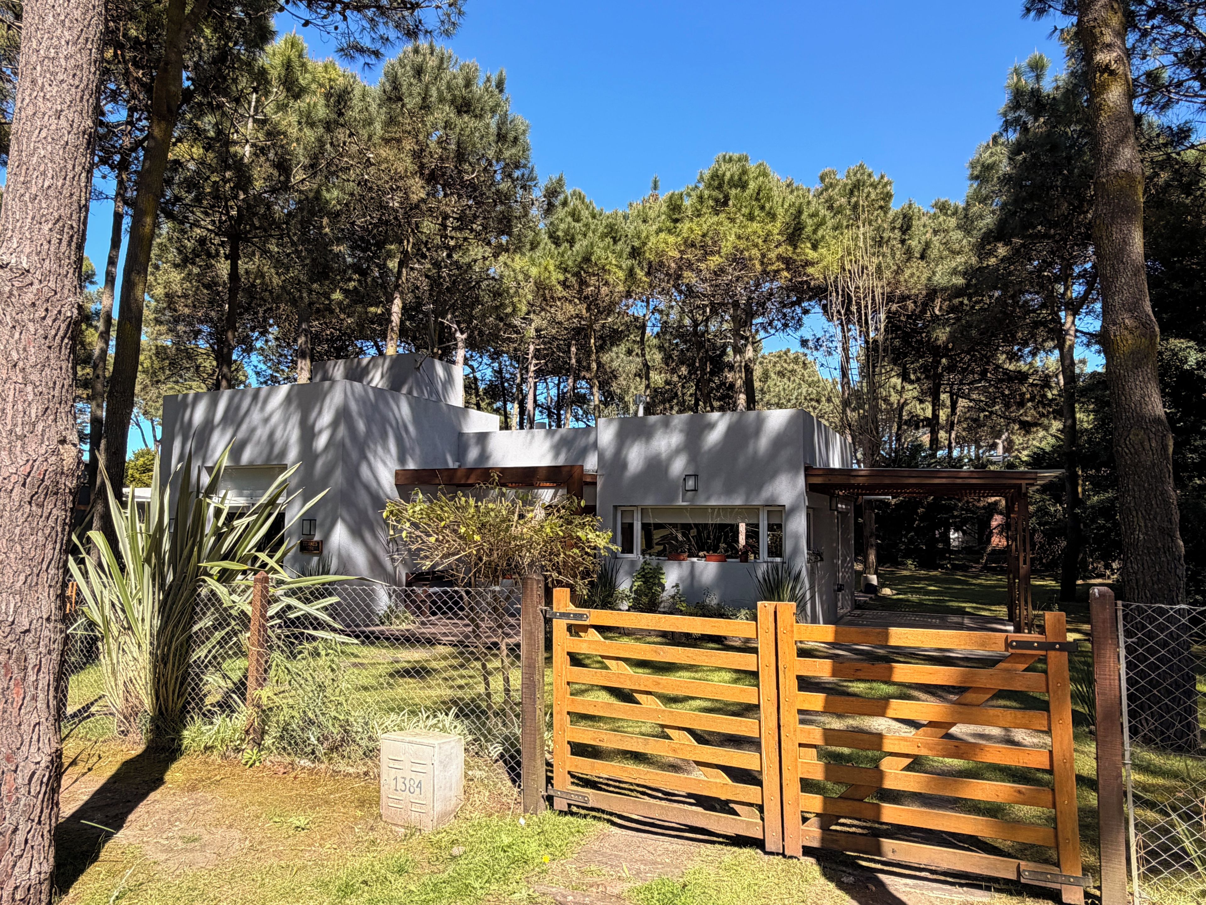 A modern building with a wooden gate, surrounded by trees and a fenced area.