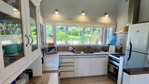 A modern kitchen with white cabinets, a wooden ceiling, and a large window overlooking a garden.