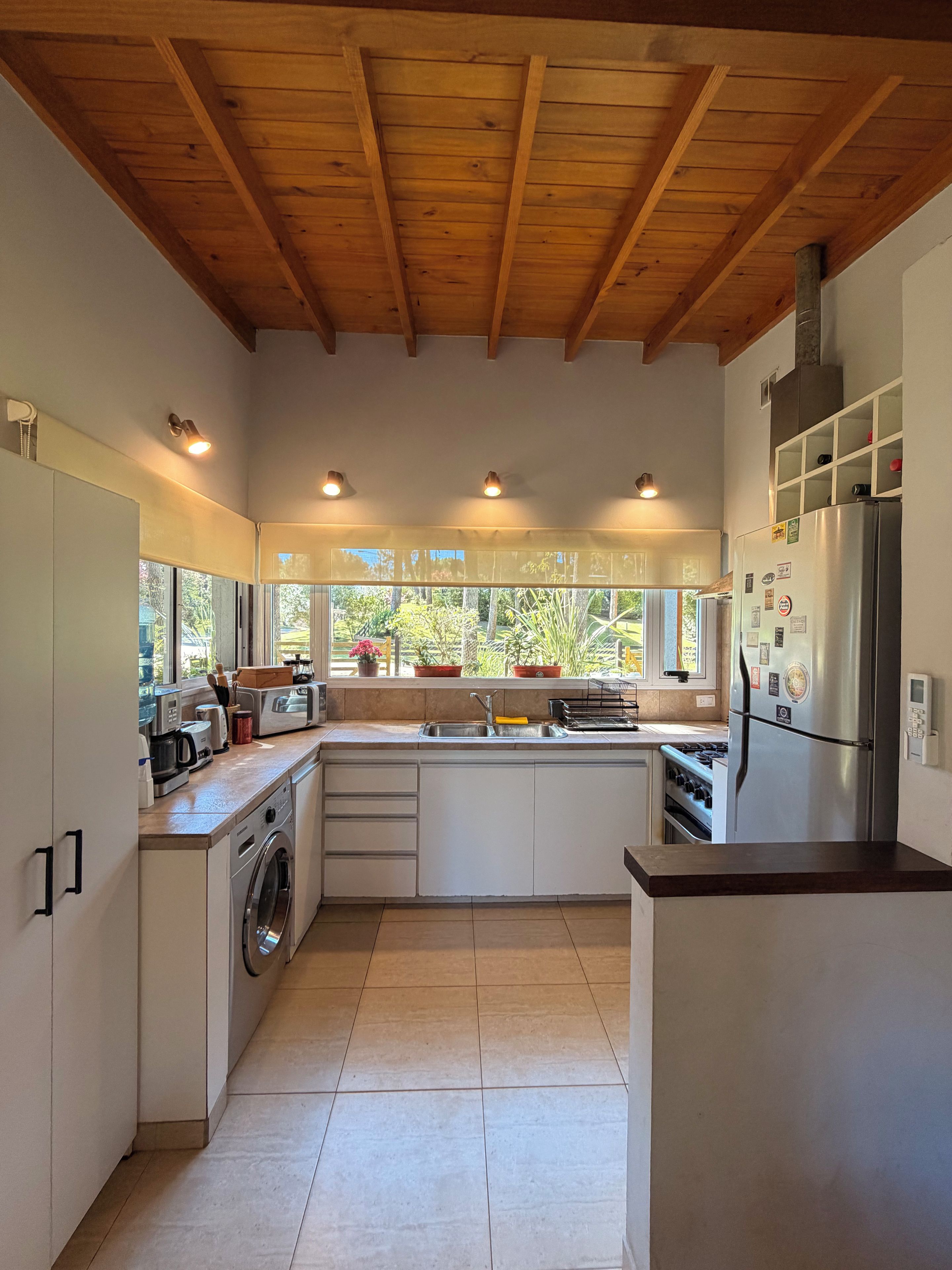 Cocina moderna con vigas de madera, lavadora integrada y refrigerador de acero inoxidable.