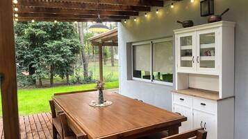 A wooden dining table with benches, a white cabinet with glass doors, and a pergola with string lights.