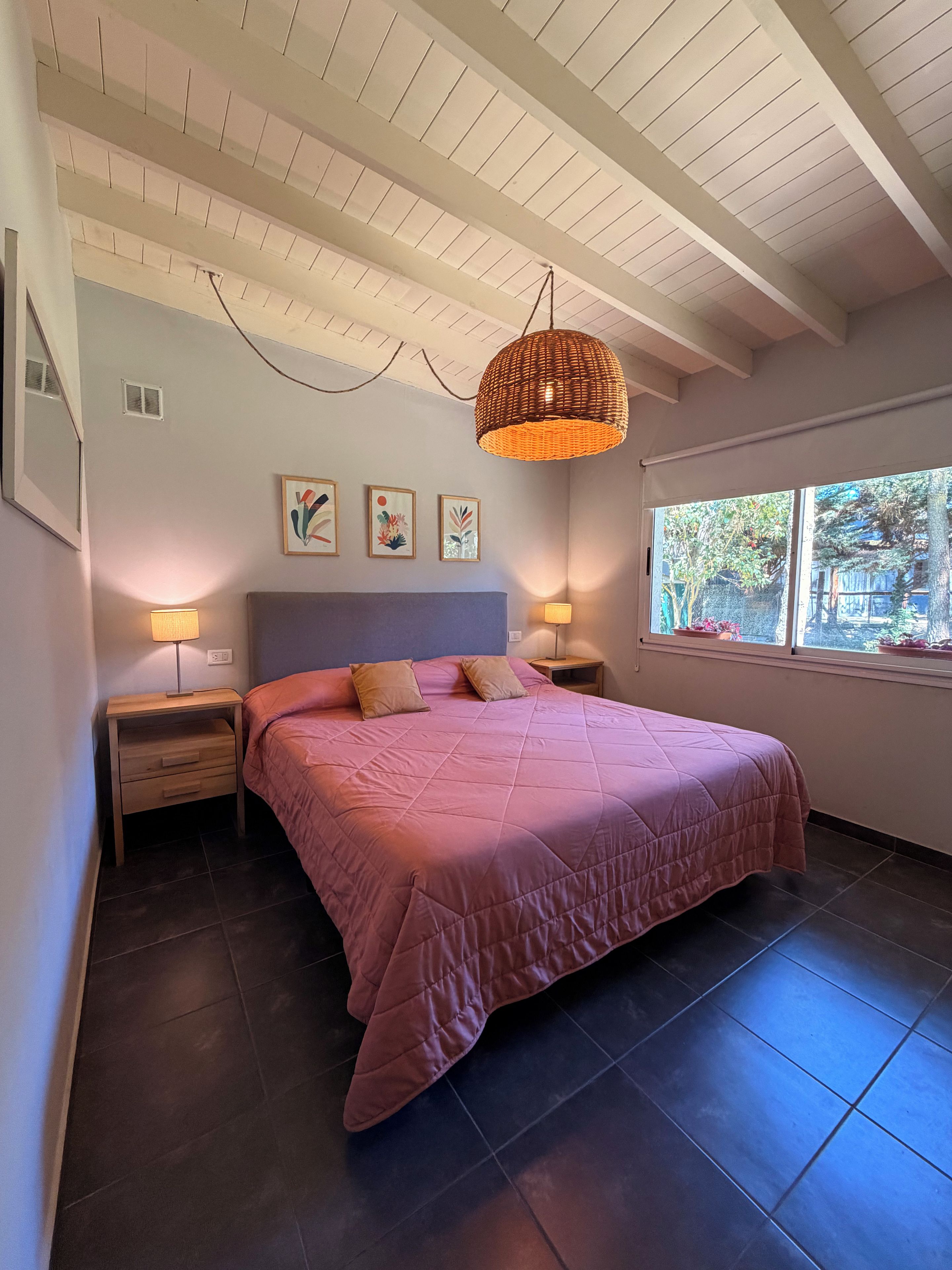 A bedroom with a large bed, two bedside tables, a ceiling fan, and a window with a view of trees.
