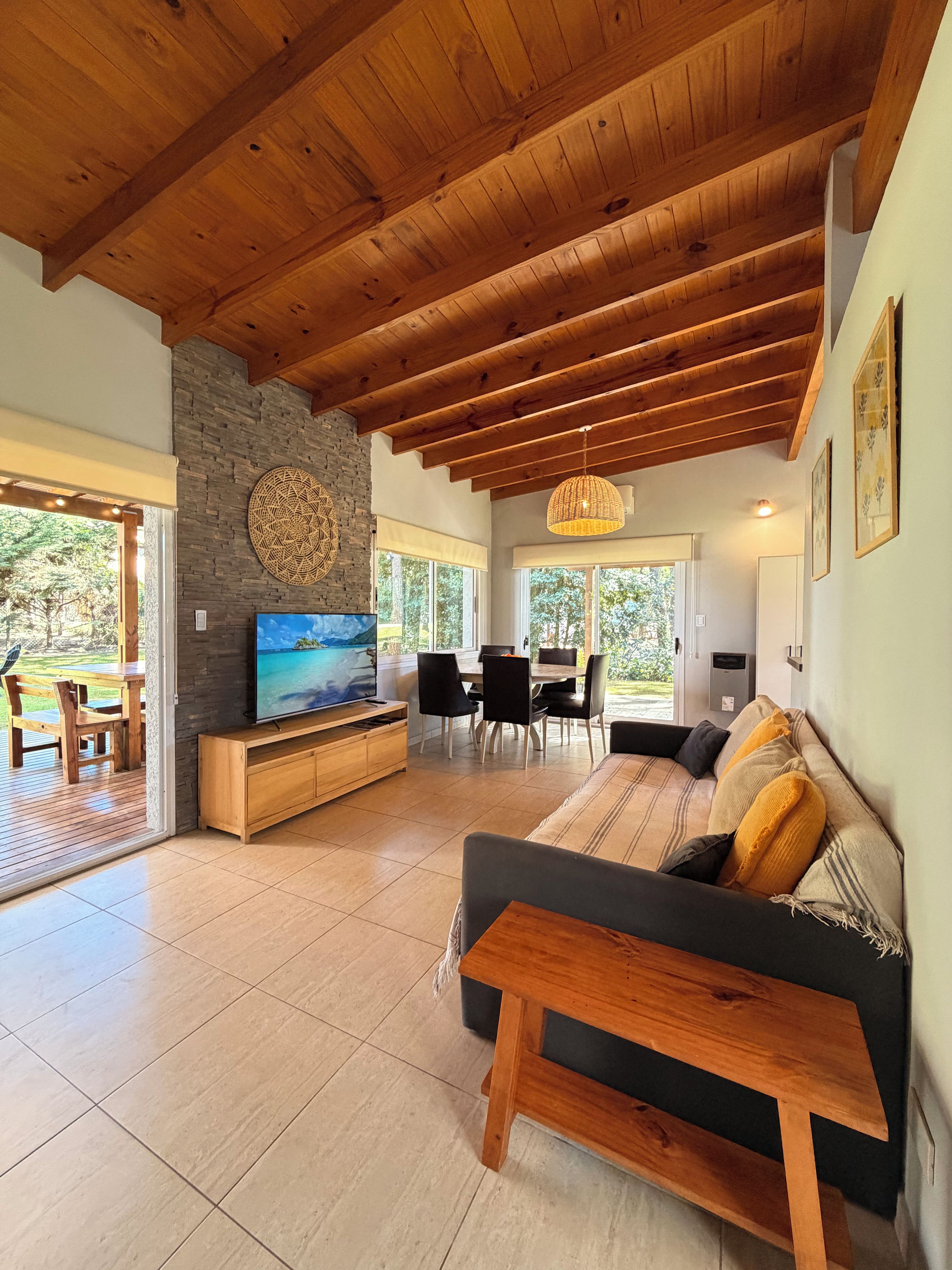 A spacious living area with a wooden ceiling, a stone wall, a television, and a dining area with chairs and a table.