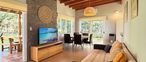 A spacious living area with a wooden ceiling, a stone wall, a television, and a dining area with chairs and a table.