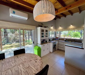 A modern kitchen with a built-in washing machine, a dining area with a round table, and large windows offering a view of the outdoors.