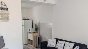 Una sala de estar moderna con un sofá negro, un televisor y una zona de cocina al fondo.