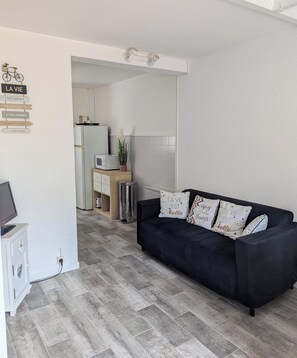 Ein modernes Wohnzimmer mit einer schwarzen Couch, einem Fernseher und einer Küche im Hintergrund.