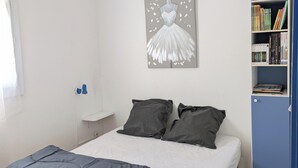 Un dormitorio con cama, almohadas, una mesita de noche, una obra de arte en la pared y una estantería.