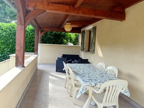 An outdoor patio with a table and chairs, a wooden ceiling, and a view of greenery. - Gîte Candéjac (Daglan)