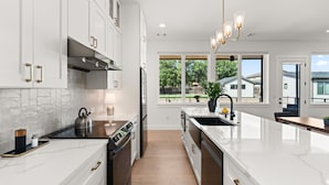 A modern kitchen with white cabinetry, stainless steel appliances, and a large island with a sink.