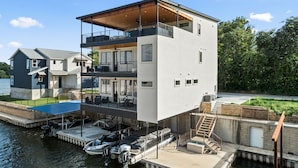A modern multi-story waterfront property with a dock, a boat, and a staircase leading to the upper levels.