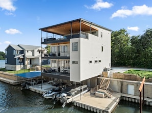 A modern multi-story waterfront property with a dock, a boat, and a staircase leading to the upper levels. - New! Lake LBJ Waterfront l 5BR Luxury Home (Kingsland)