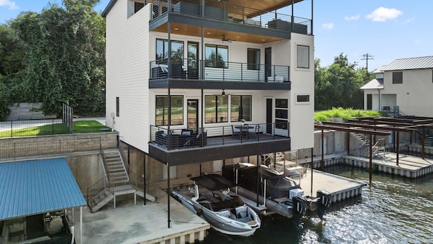 A modern two-story waterfront house with a balcony, dock, and a boat.