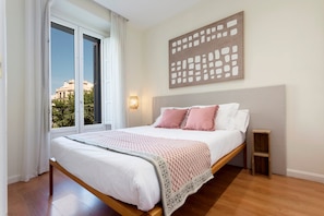 A bedroom with a bed, a window, a wall-mounted light, and a view of buildings outside. - Central 2BD Apt Facing Torre Madrid Duque de Osuna (Madrid)