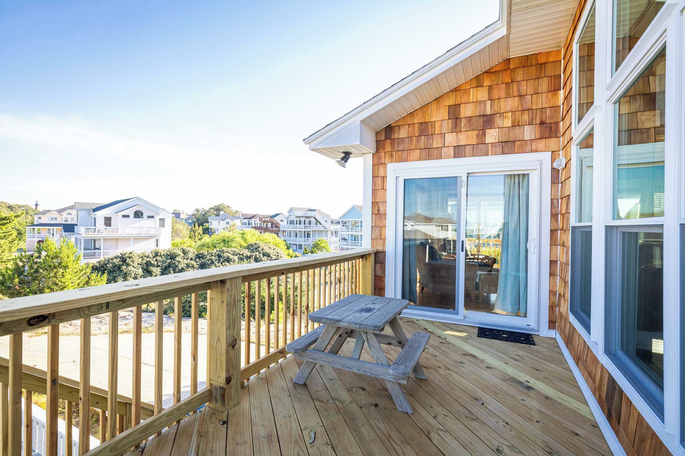 A wooden deck with a picnic table, a sliding glass door, and a view of other houses.