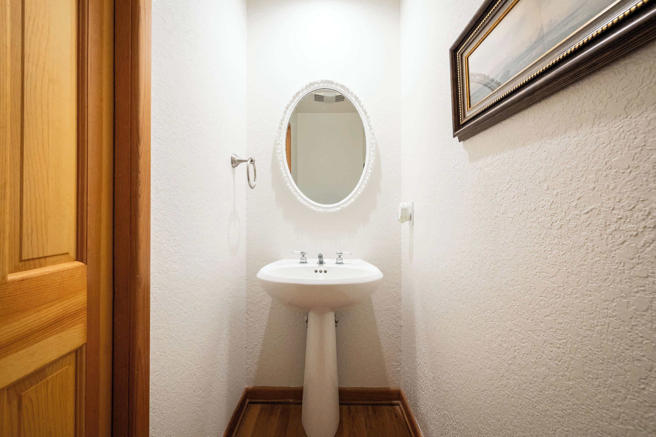 A bathroom with a pedestal sink, a mirror, and a wooden door.