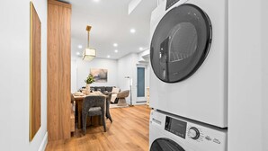 A laundry area with stacked washing machines, a dining area with a table and chairs, and a wooden floor. - The Gerrard | Group Basement CN Tower Transit Base (Toronto)