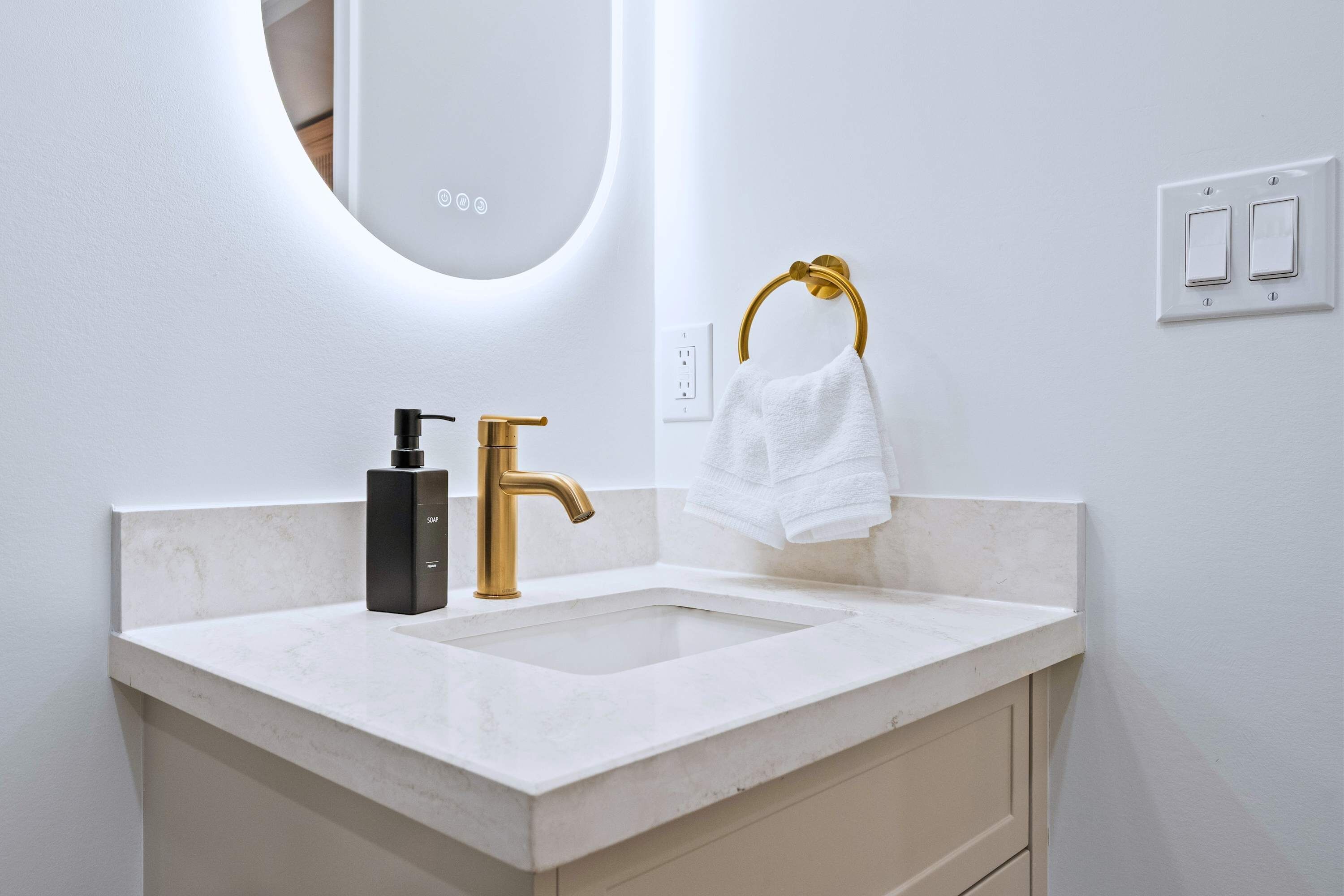 A bathroom with a white sink, gold faucet, and a towel ring.
