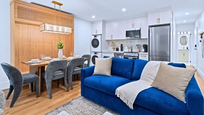 Una cocina moderna con armarios blancos, un refrigerador de acero inoxidable y un comedor con mesa de madera y sillas grises.