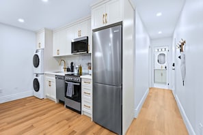 A modern kitchen with white cabinetry, stainless steel appliances, and a wooden floor. - The Gerrard | Match Day Group Stay w Patio (Toronto)