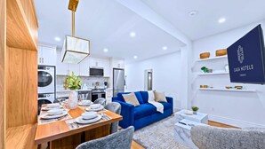 Una cocina moderna con armarios blancos, un sofá azul y un comedor con mesa de madera para cuatro.