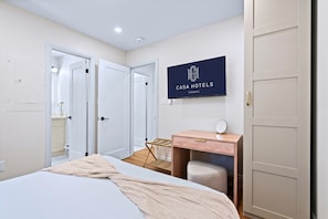 A hotel room with a bed, a desk with a chair, a mirror, and a wardrobe. - The Gerrard | Match Day Group Stay w Patio (Toronto)