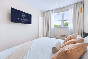 A hotel room with a bed, a TV mounted on the wall, and a window with curtains.